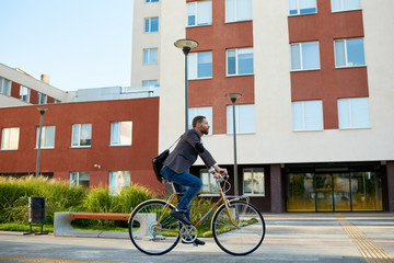 Bearded Businessman in business suit riding on retro bicycle to work on urban street in the morning...