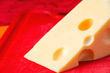Piece of cheese with holes on red board close up