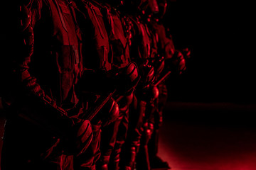 Special forces soldiers in black uniform with police batons on black background. The soldiers illuminated by red light. Only hands
