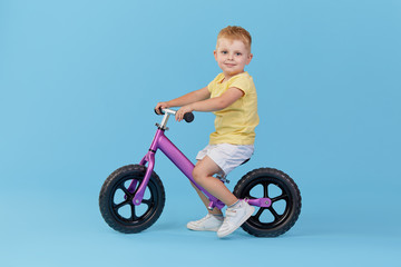 Little child boy learns to keep balance while riding a bicycle. Stylish child in yellow T-shirt on...