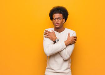 Young african american man over an orange wall going cold due to low temperature