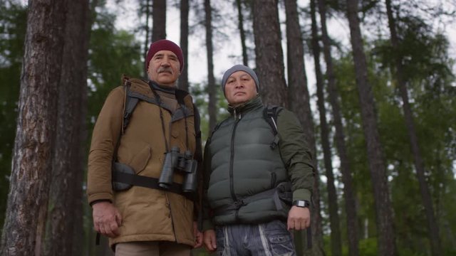 Low angled shot of two senior male hikers standing in forest and looking at camera with confidence