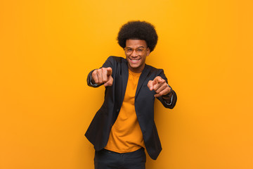 Young business african american man over an orange wall cheerful and smiling pointing to front