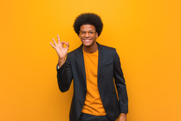 Young business african american man over an orange wall cheerful and confident doing ok gesture