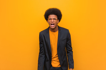 Young business african american man over an orange wall screaming very angry and aggressive