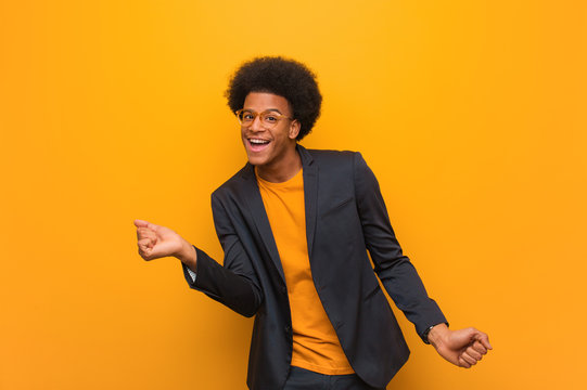 Young business african american man over an orange wall dancing and having fun