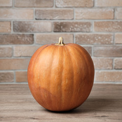 Ripe pumpkin on a wooden table on a background of defocused brick wall. Concept autumn or Halloween background