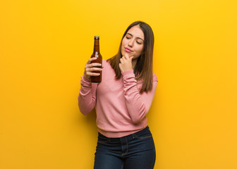 Young cute woman holding a beer doubting and confused