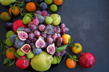 Top view. Purple figs, green figs, red grapes, pears, pomegranates, oranges and quince. Black background.