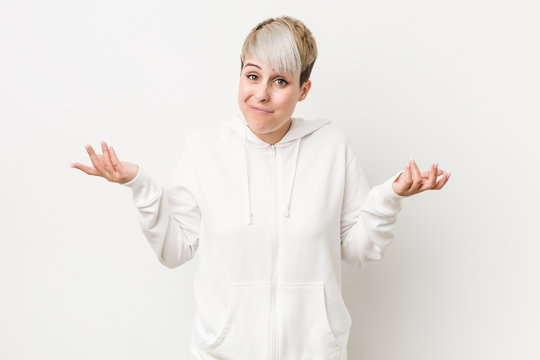 Young curvy woman wearing a white hoodie doubting and shrugging shoulders in questioning gesture.