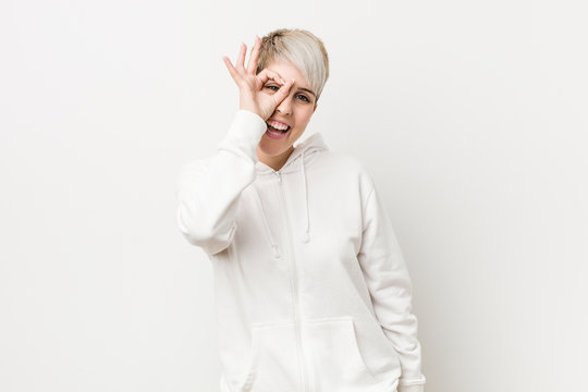 Young curvy woman wearing a white hoodie excited keeping ok gesture on eye.