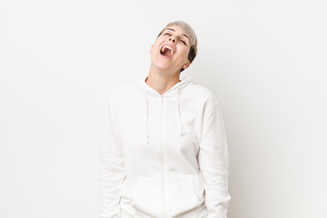 Young curvy woman wearing a white hoodie relaxed and happy laughing, neck stretched showing teeth.