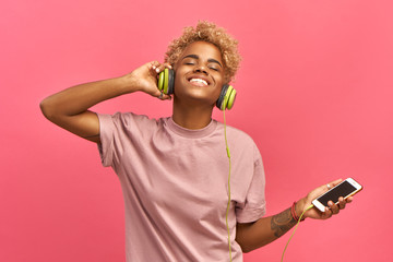 People, music, emotions concept. Delighted carefree female with Afro hairstyle dances in rhythm of...