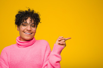 Young african american woman wearing a pink sweater smiling and pointing aside, showing something at blank space.