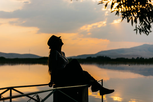 Silhouette of a model infront of a lake at sunset time, there are lots of reflections of clouds and sunset in the lake