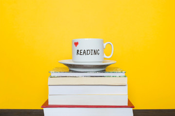 White cup with words Love reading and books on the yellow background.