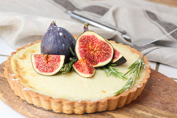 delicious round french classic homemade shortcake pastry dough vanilla custard tart cake decorated with figs and rosemary on wooden plate near with retro fork on grey table cloth. Insta food style