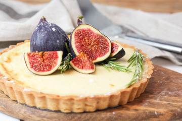delicious round french classic homemade shortcake pastry dough vanilla custard tart cake decorated with figs and rosemary on wooden plate near with retro fork on grey table cloth. Insta food style