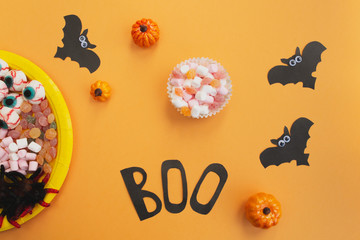 Halloween holiday concept. Halloween decorations, black paper bats, pumpkins, candy on orange background. Flat lay, top view