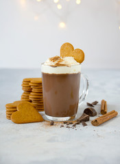 Spiced hot chocolate in glass cup with whipped cream and cinnamon next to pile of gingerbread...