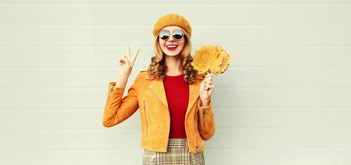 Autumn portrait Happy laughing woman with yellow maple leaves having fun wearing french beret over gray wall background