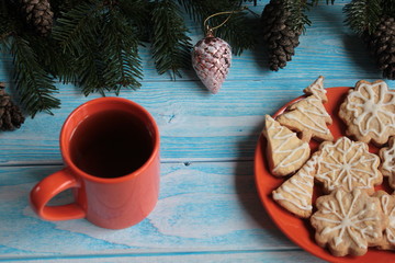 Spruce branches with cones and Christmas cookies on an orange dish on a blue wooden background.