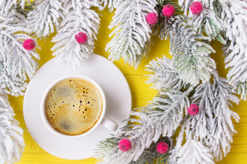 Obraz na płótnie Canvas Cup of coffee over yellow wooden planks with frosty Christmas tree branches