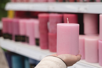 Woman holding in hands a new candle on a store counter with assortment of candles background.