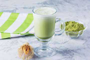 Matcha green tea latte with matcha powder and bamboo whisk. Healthy drink in a transparent glass close-up.