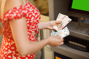 Euros banknotes and ATM machine close up. Woman taking euro money from cash machine outdoors. Female hand with euro banknotes