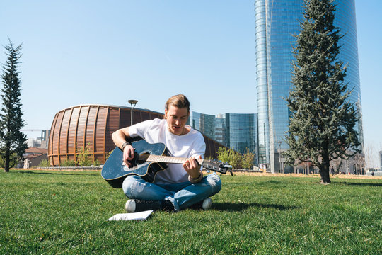 man composing music in urban garden playing guitar and reading script