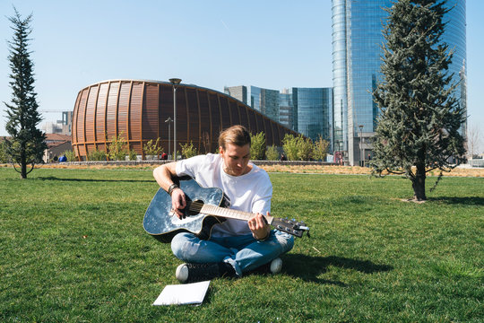 man studying music in urban garden playing guitar and reading script