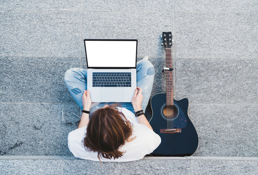 young man long hair holding laptop sitting next classical guitar