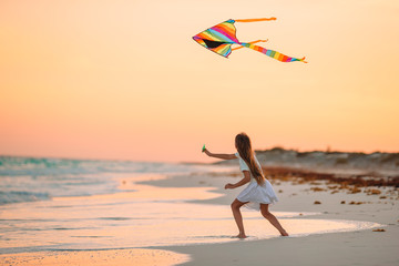 Little running girl with flying kite on tropical beach. Kid play on ocean shore.