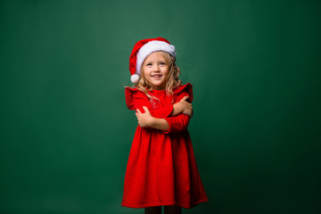 little blonde girl in Santa costume smiling on green background, space for text. merry Christmas!