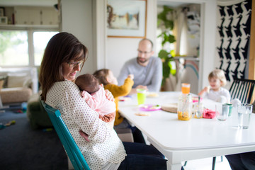 Mother holding newborn at kitchen table.