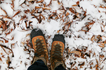 man wearing boots walking forest in autumn and winter with snow on the leaves