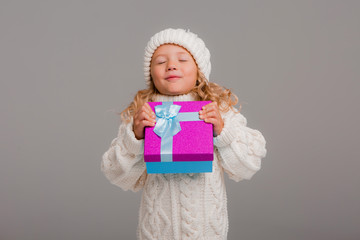 little blonde girl in winter white winter hat smiling holding a pink gift box