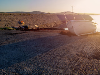 Small white plastic fishing boat on a pier at sunset, low tide. Warm colors, Sun haze. Nobody,