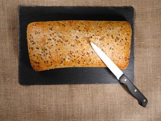 Sourdough bread on a slate plate with knife on hessian table cloth.