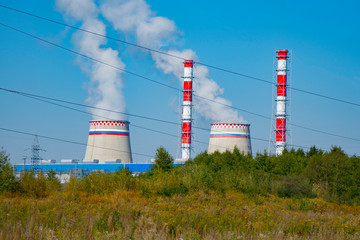 the smoky chimneys of the power plant stand against the blue sky