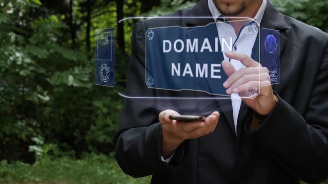 Unrecognizable businessman activates conceptual HUD holograms on smartphone with text Domain name. Bearded man in a white shirt and a jacket with a holographic screen on a background of green trees