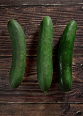 Three dark green whole cucumbers on dark wooden board, view from above