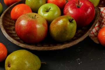 Apples, pears and orange tangerines on wooden carved bowl - closeup detail