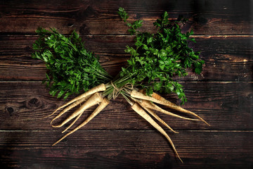 Two bunch of parsley with green leaves crossed, on dark wooden board, view from above