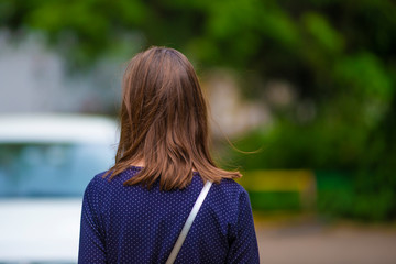Rear view of the female hairstyle long wavy bob. Young woman stands against a yellow blooming spring bush, her hair shining in the sun.