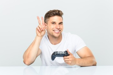 Young man holding a game controller showing victory sign and smiling broadly. © Asier