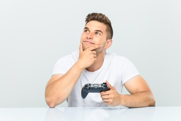 Young man holding a game controller looking sideways with doubtful and skeptical expression. © Asier