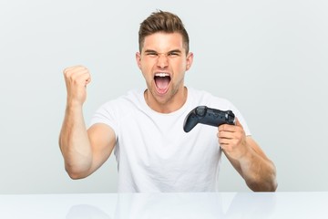 Young man holding a game controller cheering carefree and excited. Victory concept. © Asier