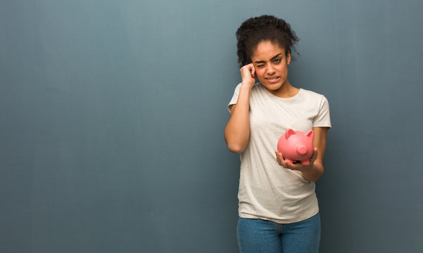 Young Black Woman Covering Ears With Hands. She Is Holding A Piggy Bank.